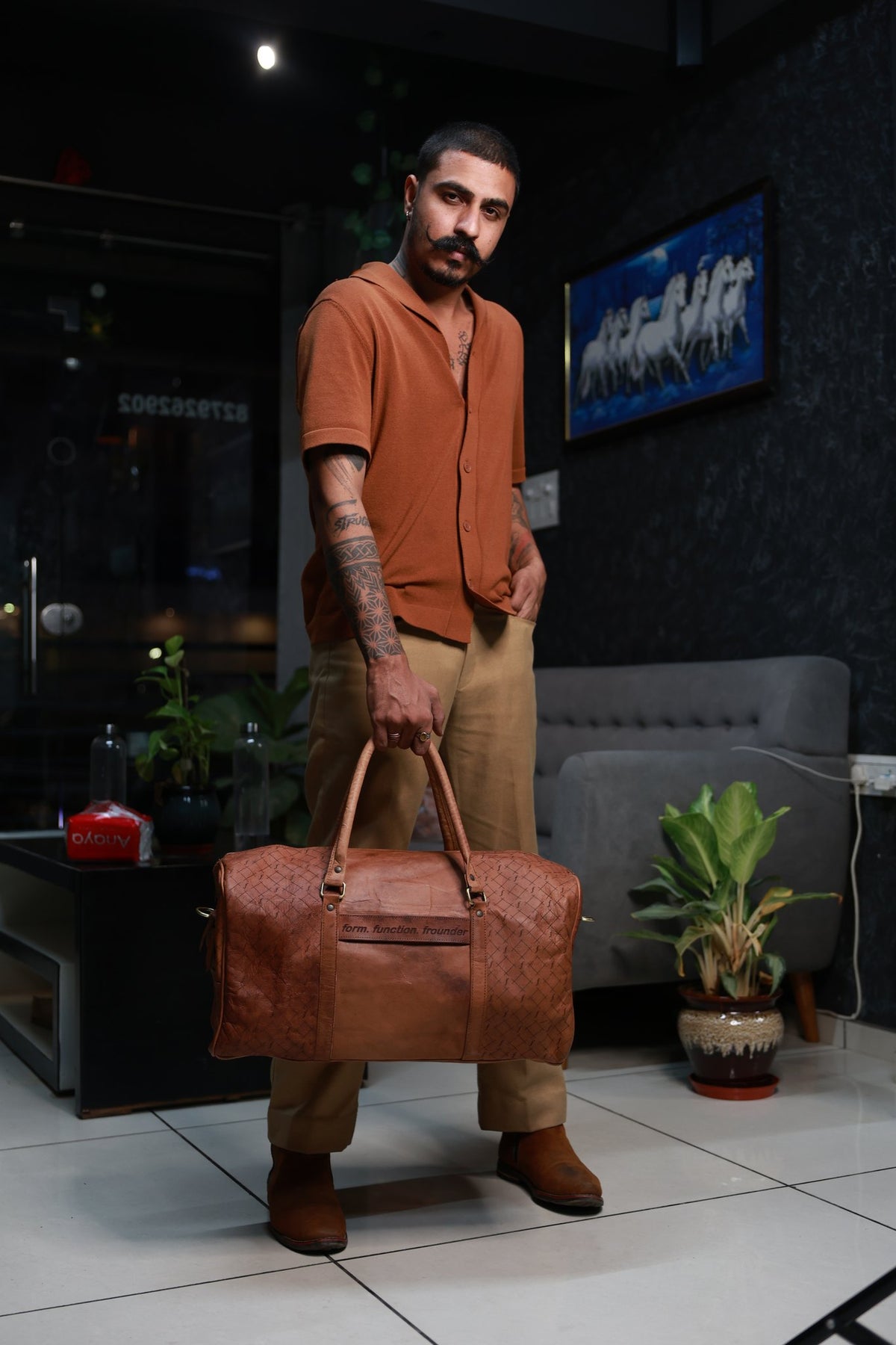 Man in a rust shirt carrying the Frounder Orion tan leather weekender duffel by its top handles