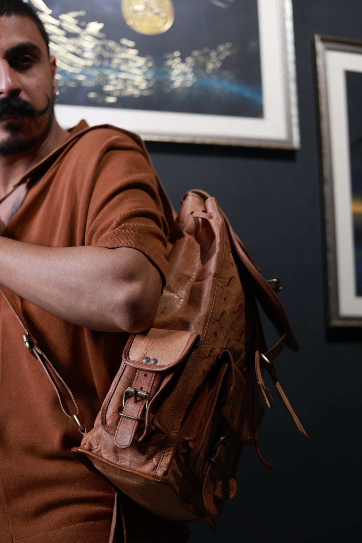The Helios leather backpack carried over one shoulder, buckled flap closed