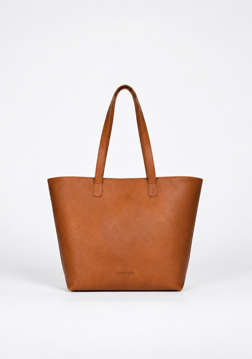 A structured tan leather tote bag with dual shoulder straps and a subtle embossed brand name near the bottom center, photographed against a clean white studio background.