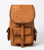 A tan leather backpack with a textured ostrich-style print on the flap and front pocket, featuring brass-tone hardware and a central buckle strap, photographed against a clean white background.