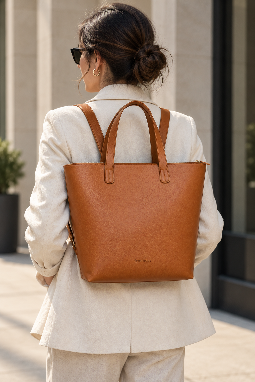 Woman carrying the Frounder Polaris 2-in-1 leather tote worn as a backpack, showing the embossed Frounder mark low on the front panel